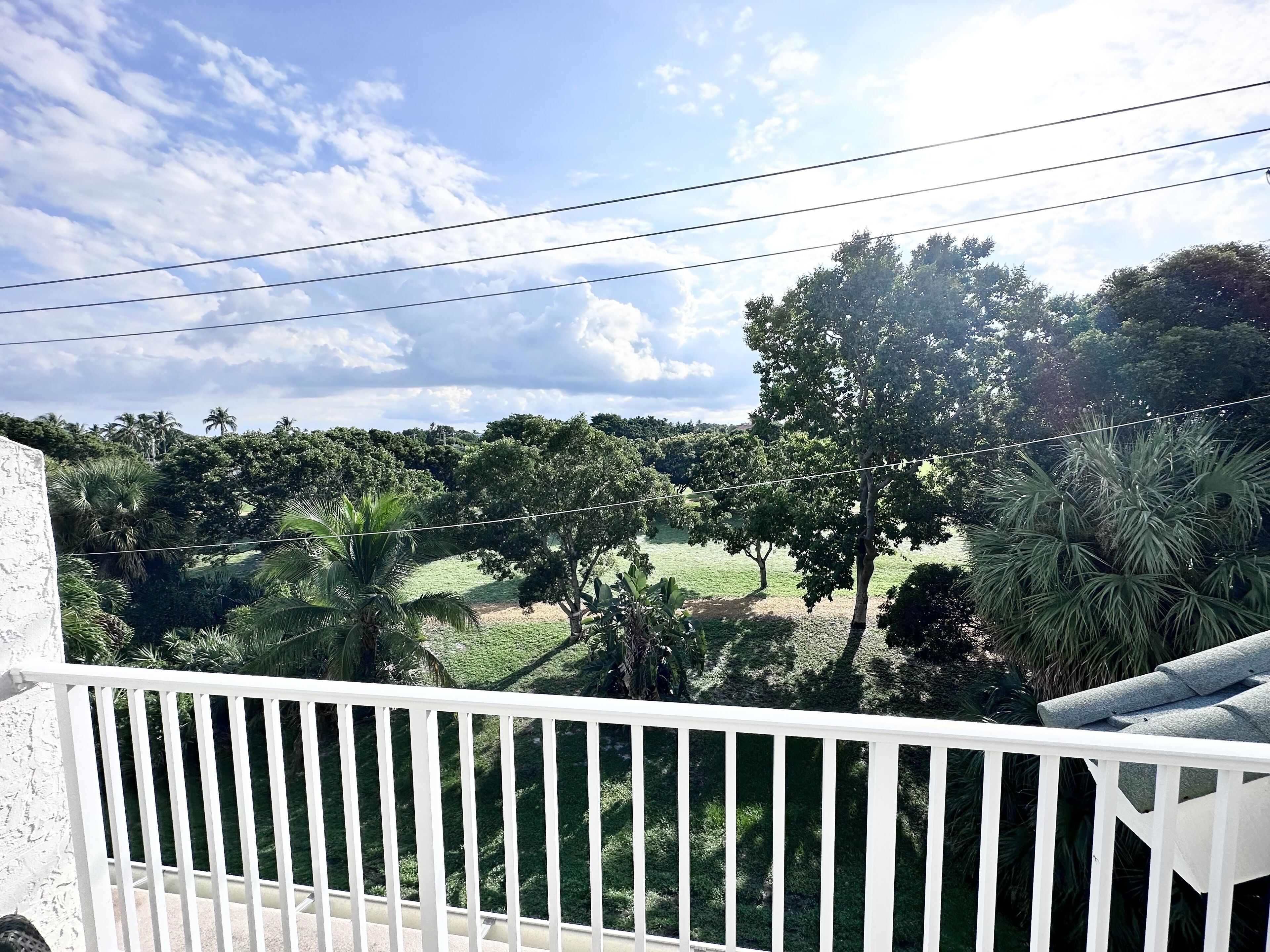 A balcony with a white railing overlooking a lush green landscape with trees and a clear sky.