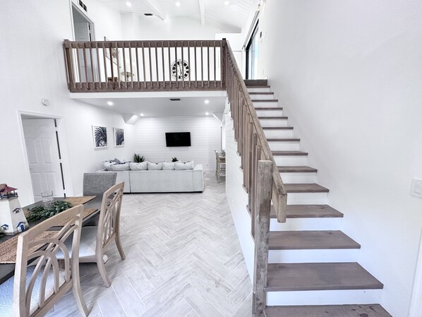 Un vaste espace de vie doté d’un parquet à motifs en chevrons, d’un grand canapé gris, d’une table à manger avec des chaises et d’un escalier en bois muni d’une rampe.