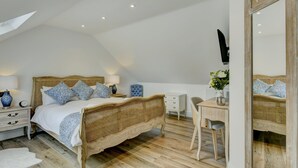 Une chambre à coucher avec un lit en rotin, des tables de chevet blanches, un bureau en bois et un grand miroir.