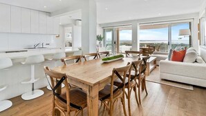 Una cocina moderna con armarios blancos, una mesa de comedor de madera y vistas a la ciudad a través de amplios ventanales.