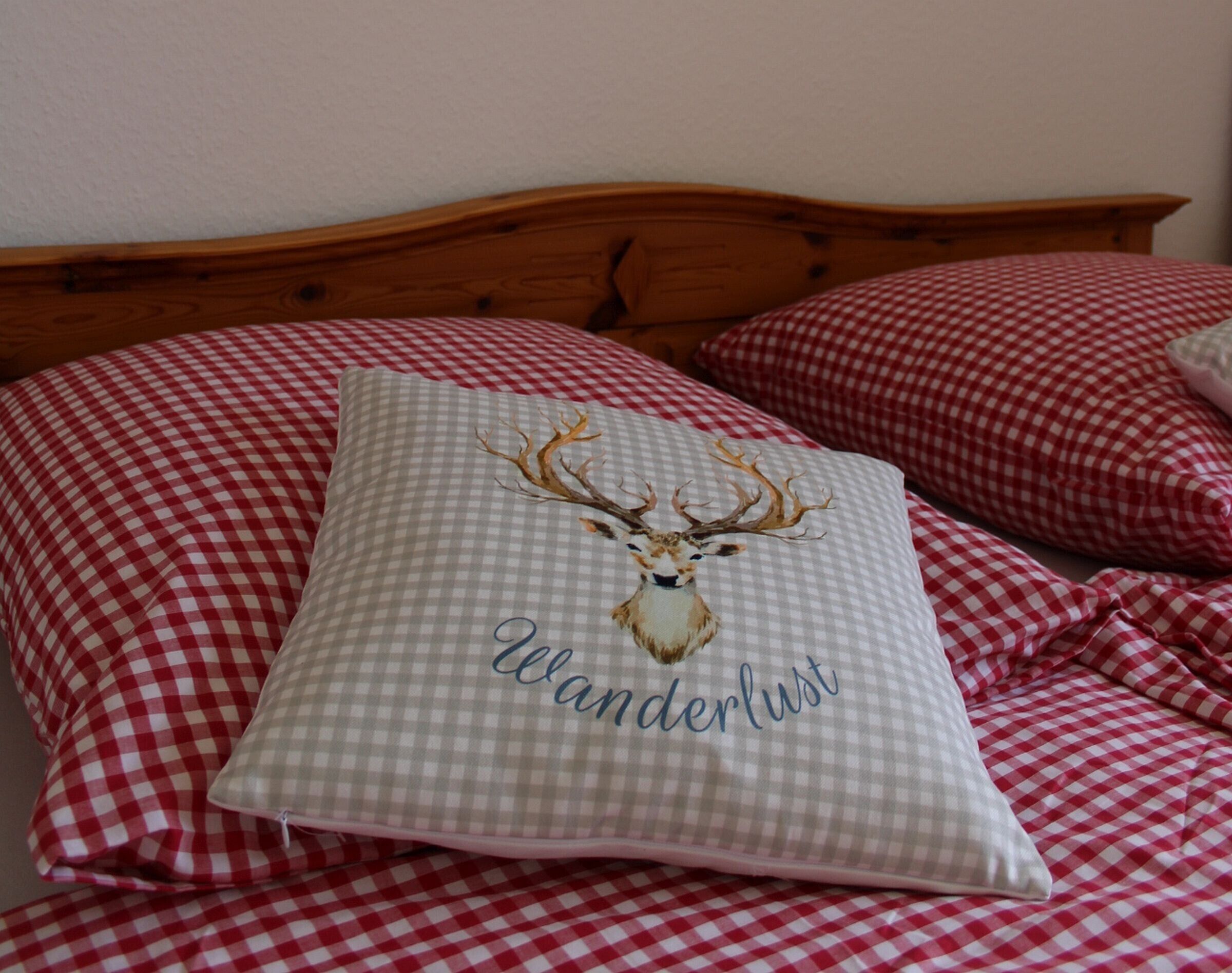 Un letto con copriletto a quadri, un cuscino con l'illustrazione di una cerva e la scritta 'Wanderlust', e una testiera in legno.