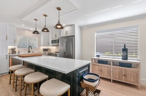 A modern kitchen with white cabinetry, stainless steel appliances, and a central island with stools.