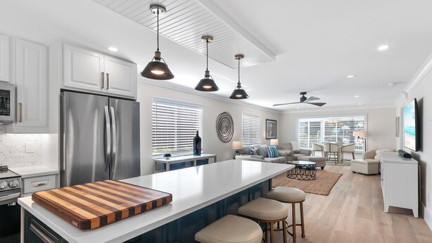 A modern kitchen with a large island, stainless steel appliances, pendant lighting, and a seating area with a sofa and chairs. - RENOVATED 2 Bed, 2 Bath 1st floor with heated pool on the bay! (Naples)