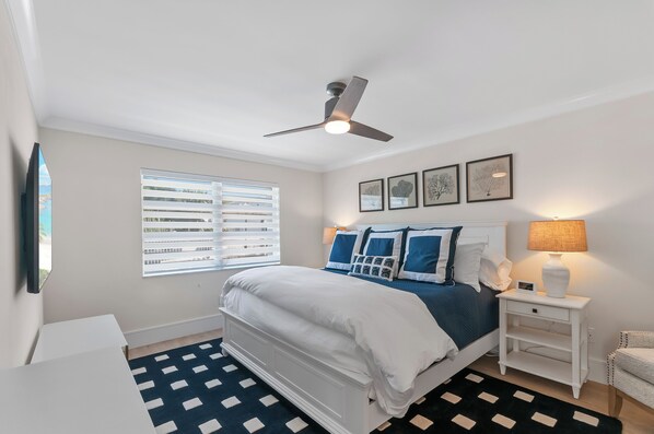 A bedroom with a bed, a nightstand, a lamp, a ceiling fan, and a window with blinds.