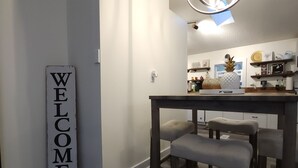 Une cuisine moderne avec une table à manger et un banc, une pancarte « BIENVENUE » et un luminaire suspendu.
