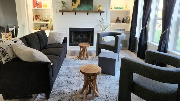 Un salon avec une cheminée, un canapé noir, un fauteuil gris et une petite table en bois.