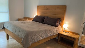 A bedroom with a wooden bed, a nightstand with a lamp, and a window with blinds.