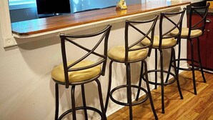 A kitchen with a bar area, wooden bar stools, a ceiling fan, and a television in the background.