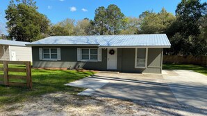 A single-story house with a metal roof, a front porch, and a driveway leading to the entrance.