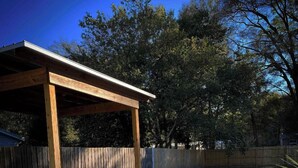 A covered patio area with a fire pit and a wooden fence in the background.