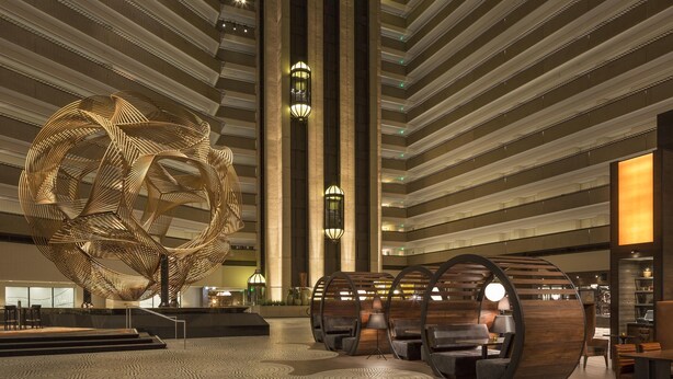 A spacious lobby with a large abstract sculpture, tiered seating, and modern lighting fixtures.