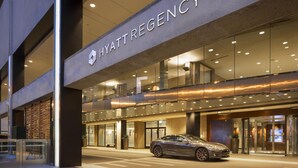 A modern hotel entrance with a car parked in front, glass doors, and a sign reading 'HYATTREGENCY'.