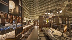 A modern bar area with a long counter, seating, and a unique ceiling design.