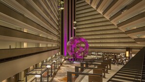 Eine großzügige Hotelhalle mit einer zentralen Treppe, Sitzbereichen und einer auffälligen, violetten Skulptur.