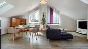 A modern loft apartment with a dining area, a sofa, a TV, and a large window with curtains.