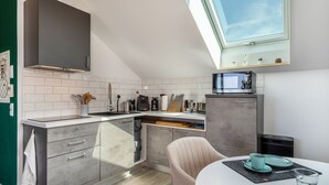 A modern kitchen with a skylight, white tiles, grey cabinets, and a dining area with a table and chairs.