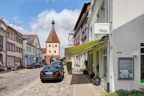 Eine Kopfsteinpflasterstraße mit historischen Gebäuden, einem Glockenturm und einem Schild für ein Hotel namens 'Ferienwohnung am TOR'.