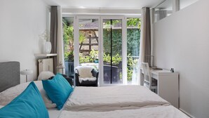 Ein Schlafzimmer mit Bett, Schreibtisch, Stuhl und Blick ins Freie durch eine Schiebetür.