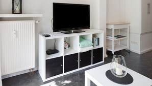 Ein modernes Wohnzimmer mit einem Flachbildfernseher auf einer weißen Unterhaltungseinheit, einem Glastisch mit einer Kerze und einer Heizung.