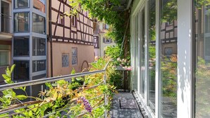 Ein schmaler Balkon mit Metallgeländer, Blick auf angrenzende Gebäude und eine kleine Gartenanlage mit Pflanzen und Blumen.