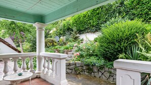 Een overdekt buitengebied met een witte balustrade, een stenen muur en weelderige begroeiing.