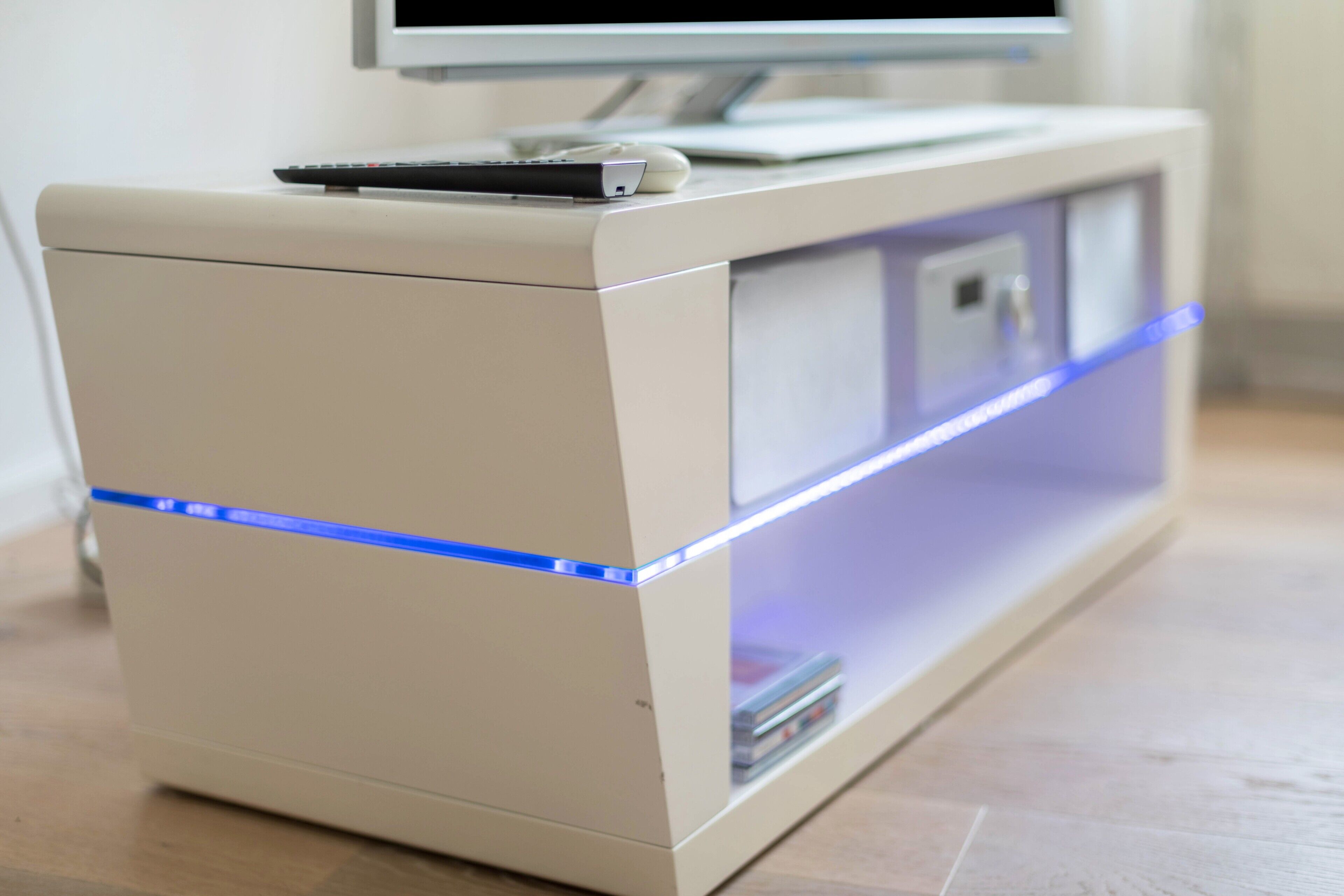 Ein moderner, minimalistischer TV-Schrank mit einem Flachbildfernseher darauf, einer Fernbedienung und einem kleinen Regal mit Büchern.