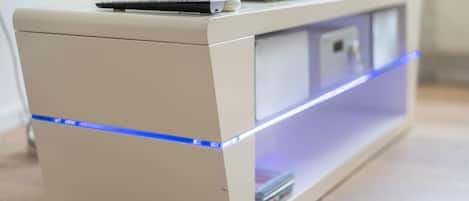 A modern, minimalist TV stand with a flat-screen TV on top, a remote control, and a small shelf with books.