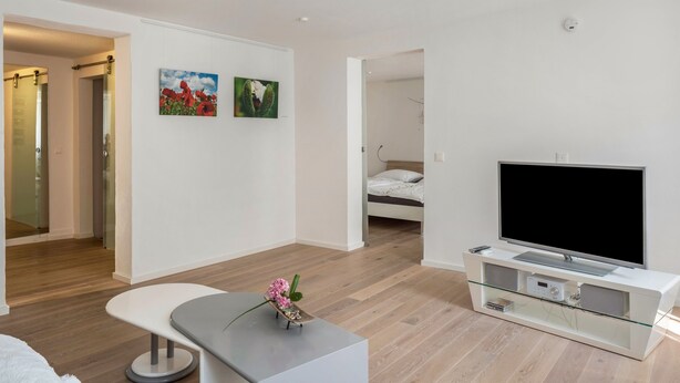 A modern living room with a flat-screen TV, a glass coffee table, and a white sofa.