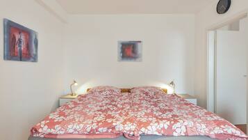 A bedroom with a bed, two bedside lamps, a wall clock, and two pieces of wall art.