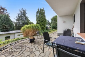 A patio area with a stone floor, a potted plant, a chair, and a table with a book and a glass object. - Apartment 'Oreste' with Private Terrace, Private Garden and Wi-Fi (Overath)