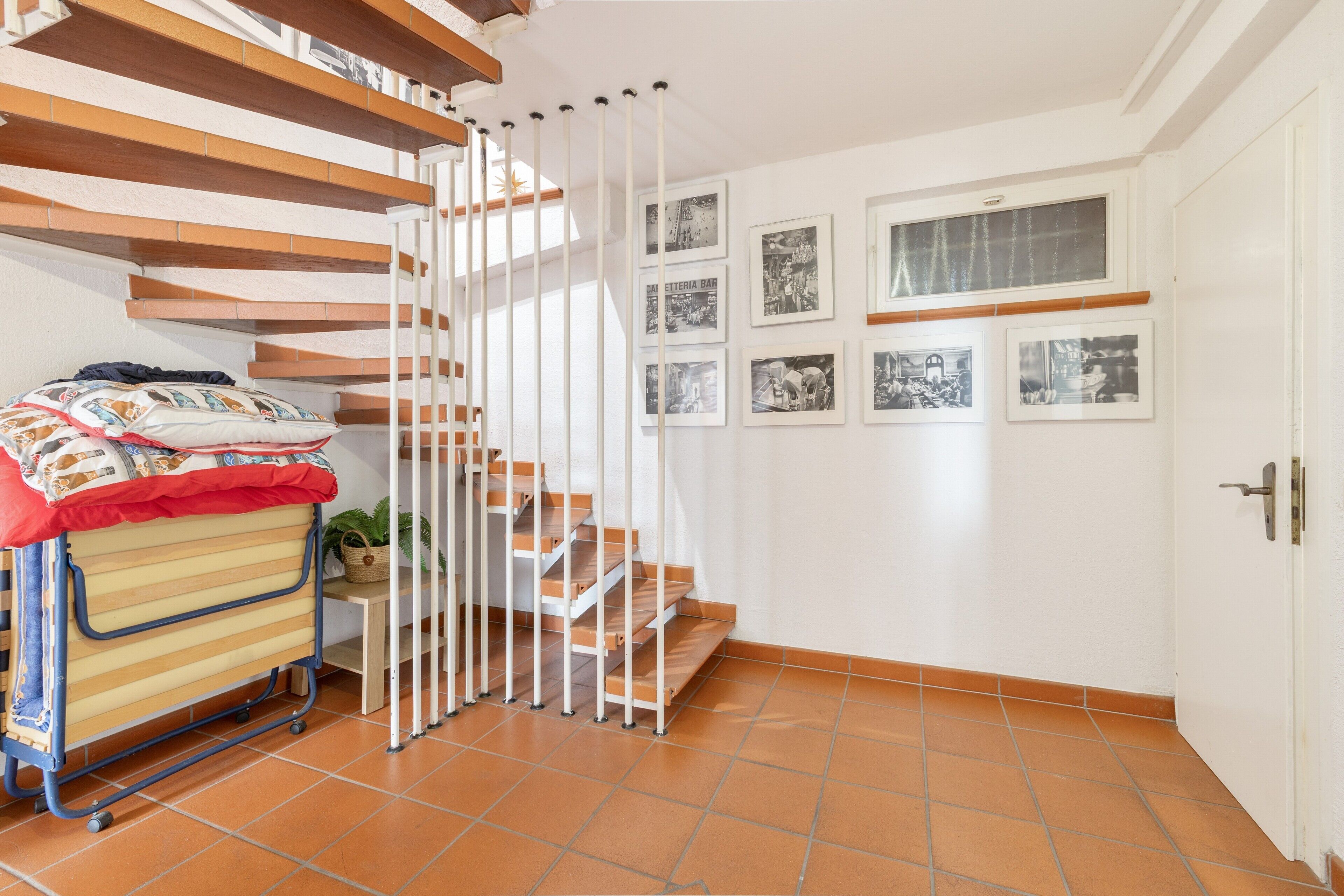 Ein Zimmer mit einem Bett, einem kleinen Tisch mit einem Korb, einem Stuhl und einer Treppe mit Geländer.