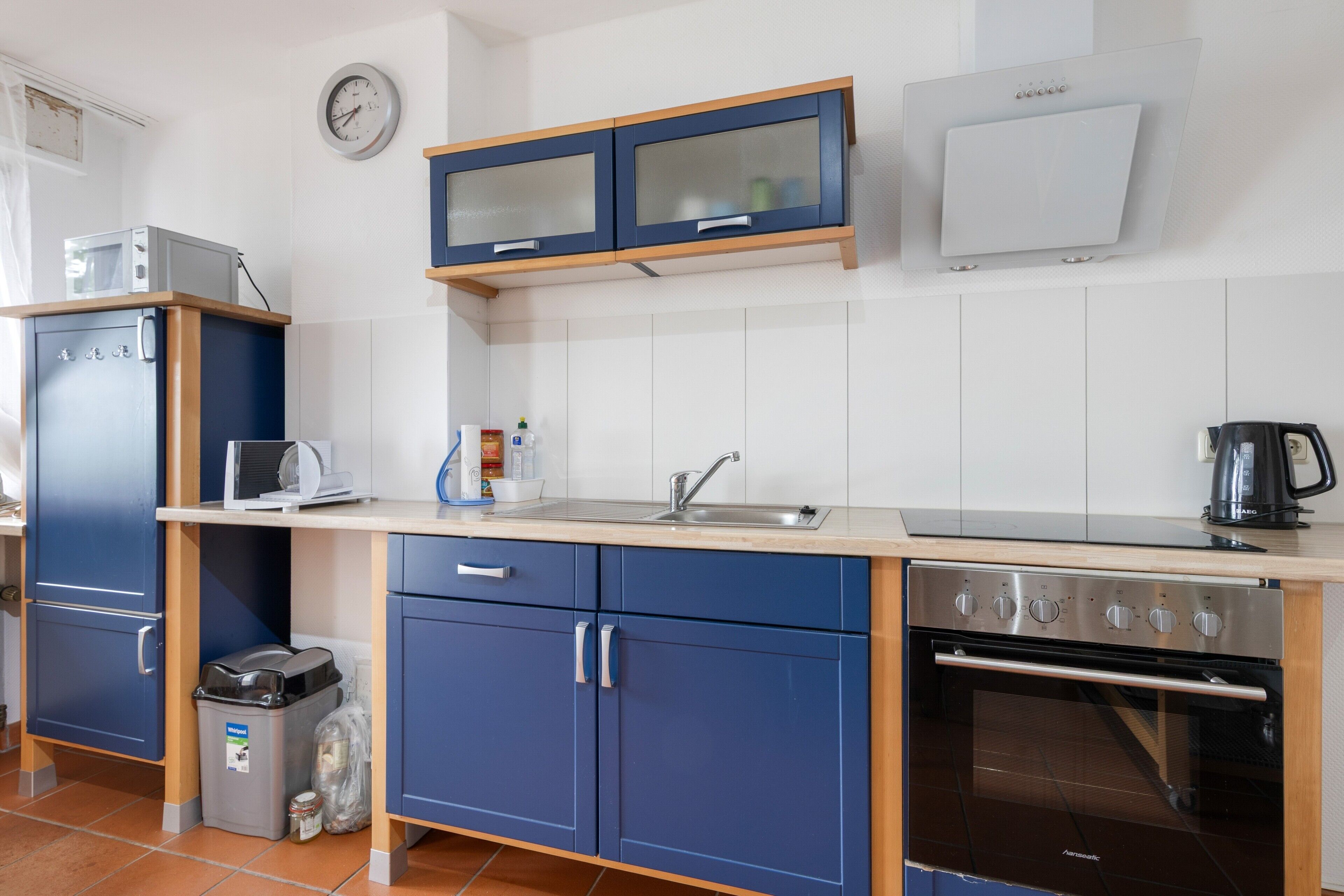 A modern kitchen with blue cabinets, a stainless steel oven, a microwave, and a coffee maker.