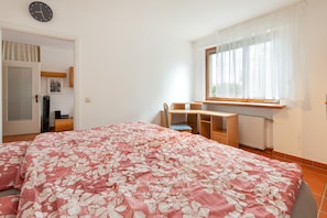 A bedroom with a bed, a desk, a chair, a radiator, and a window with curtains.