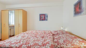 A bedroom with a bed, a wardrobe, a desk, and a painting on the wall.