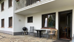 Un patio con suelo de piedra, una parrilla, sillas y una mesa.