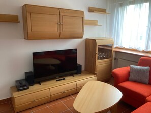 A living room with a TV, wooden cabinets, a glass cabinet, a red sofa, and a small table.