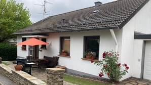 Una casa con patio de piedra, una parrilla y un comedor con mobiliario de exterior.