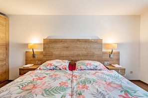 Ein Hotelzimmer mit einem hölzernen Kopfteil, floralem Bettbezug, Nachttischlampen und einem roten Kopfkissen.