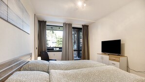 Habitación de hotel con una cama, un televisor sobre un mueble de madera, un escritorio y una ventana con cortinas.