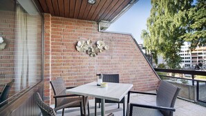 Un balcón con pared de ladrillo, sillas de mimbre, una mesa y un adorno mural.