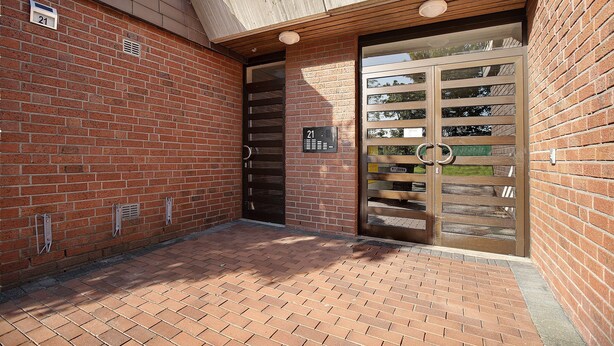 Un edificio de ladrillo con una puerta numerada, un ventanal pequeño y una rejilla metálica.