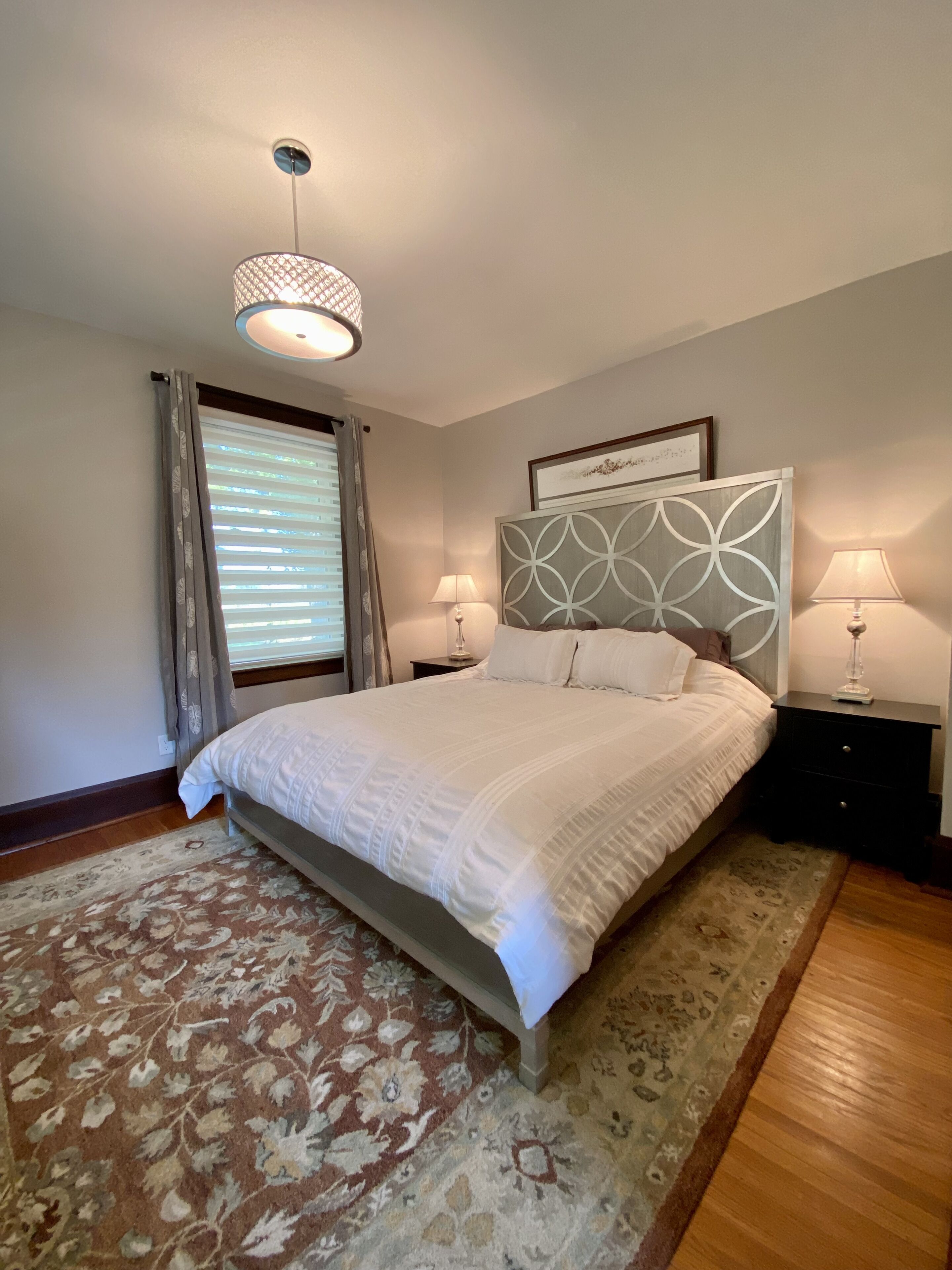 Une chambre à coucher bien aménagée, avec un grand lit, deux tables de chevet avec des lampes, un tapis à motifs et un luminaire au plafond.