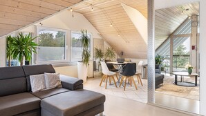 Ein modernes Interieur mit schrägverdeckter Decke, einem Essbereich mit rundem Tisch und Stühlen sowie einer Couch mit gemusterten Kissen.
