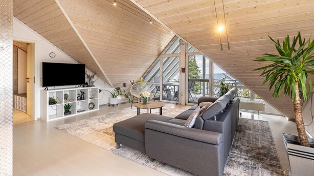 Ein modernes Wohnzimmer mit einem großen, grauen Ecksofa, einem Flachbildfernseher und einer Holzbalkendecke.