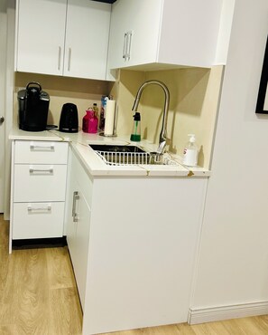 A compact kitchen with white cabinets, a sink, a kettle, and a soap dispenser.