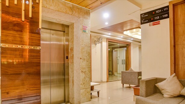 Een hotel lobby met een houten receptiebalie, een zithoek met een bank, en een lift.