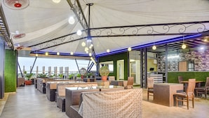 Een terrasrestaurant op het dak, met buitenplaatsen, overdekt door een groot wit dakzeil en voorzien van moderne verlichting en decoratieve details.