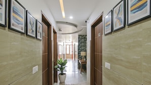 A hallway with wooden doors, framed artwork on the walls, a potted plant, and a rug on the floor. - Fabhotel Meridian Inn (Kharar)