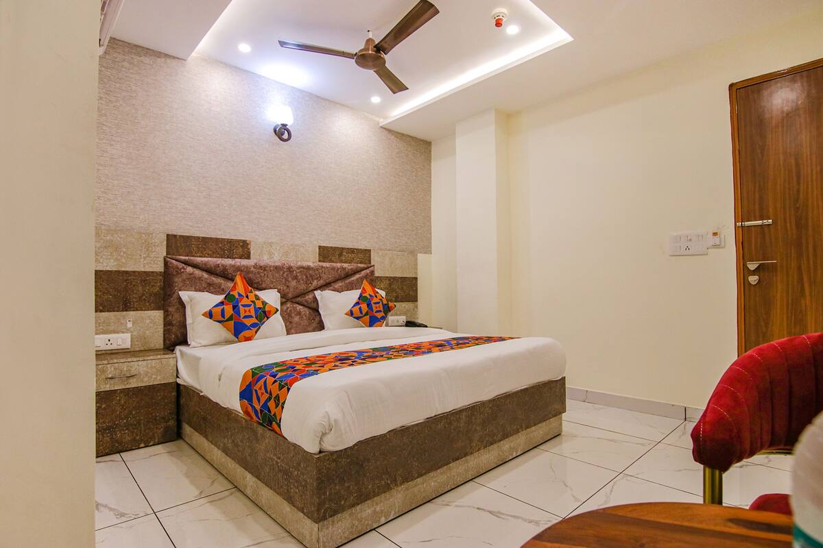 A hotel room with a bed, a ceiling fan, a nightstand, and a red chair.