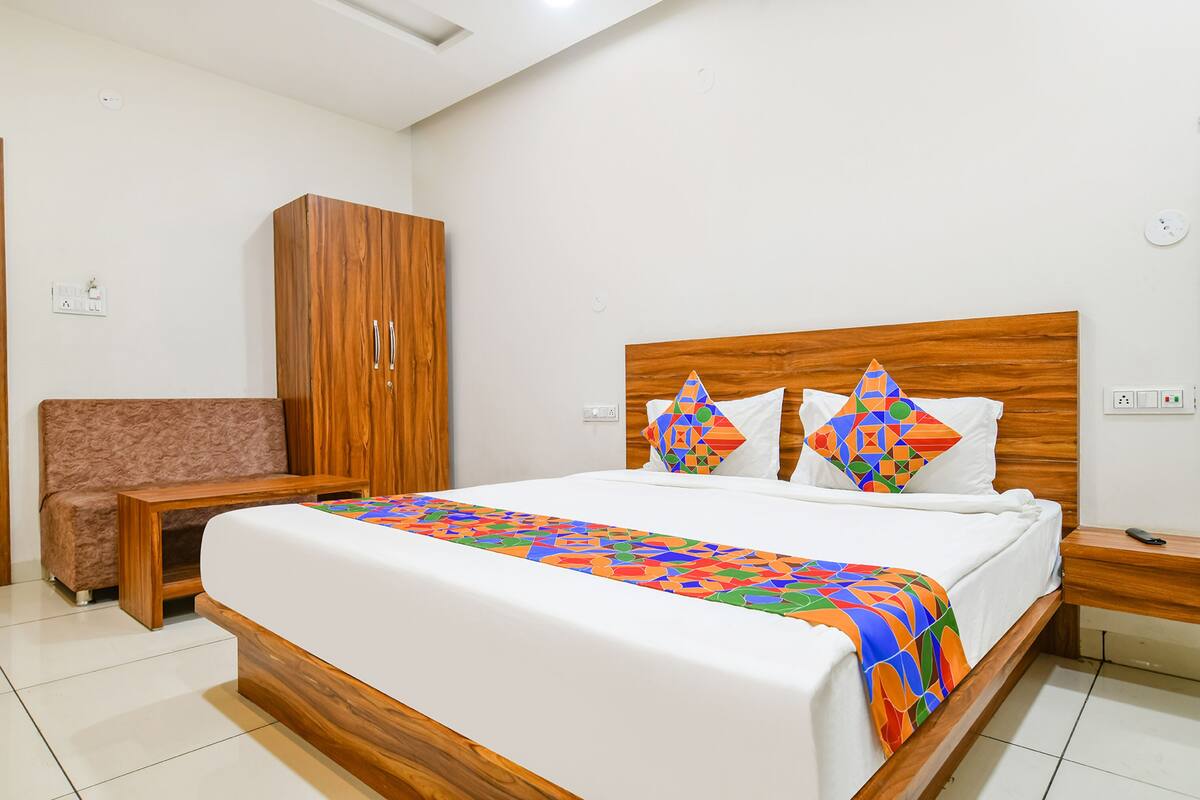 Un dormitorio ordenado con cabecero de madera, una mesita de noche a juego, un armario de madera y una silla con cojín.